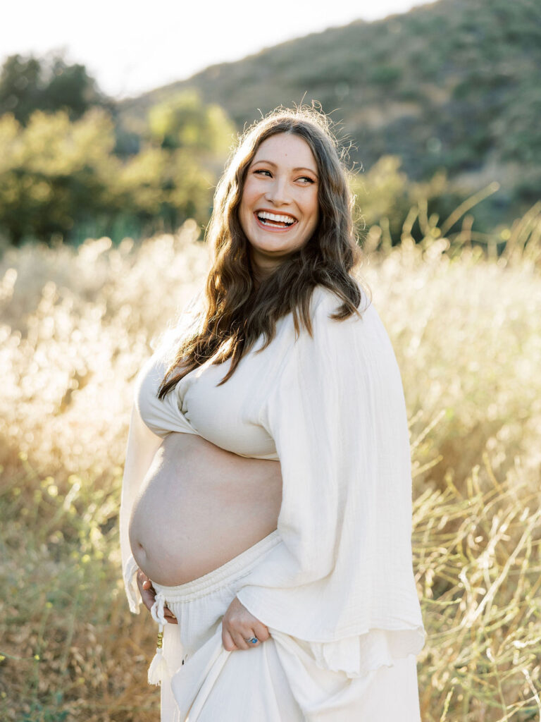 When to Take Maternity Photos with a smiling pregnant woman posing in a golden Santa Clarita field