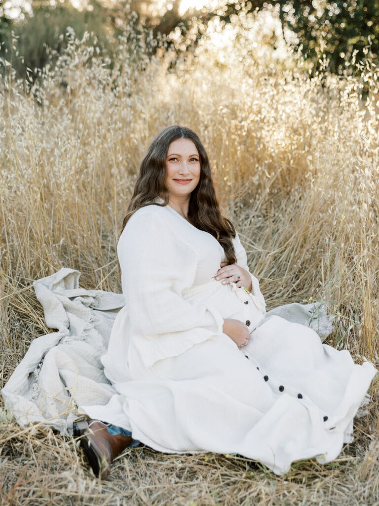 Pregnant woman seated in a golden field cradling her belly during a Santa Clarita maternity session