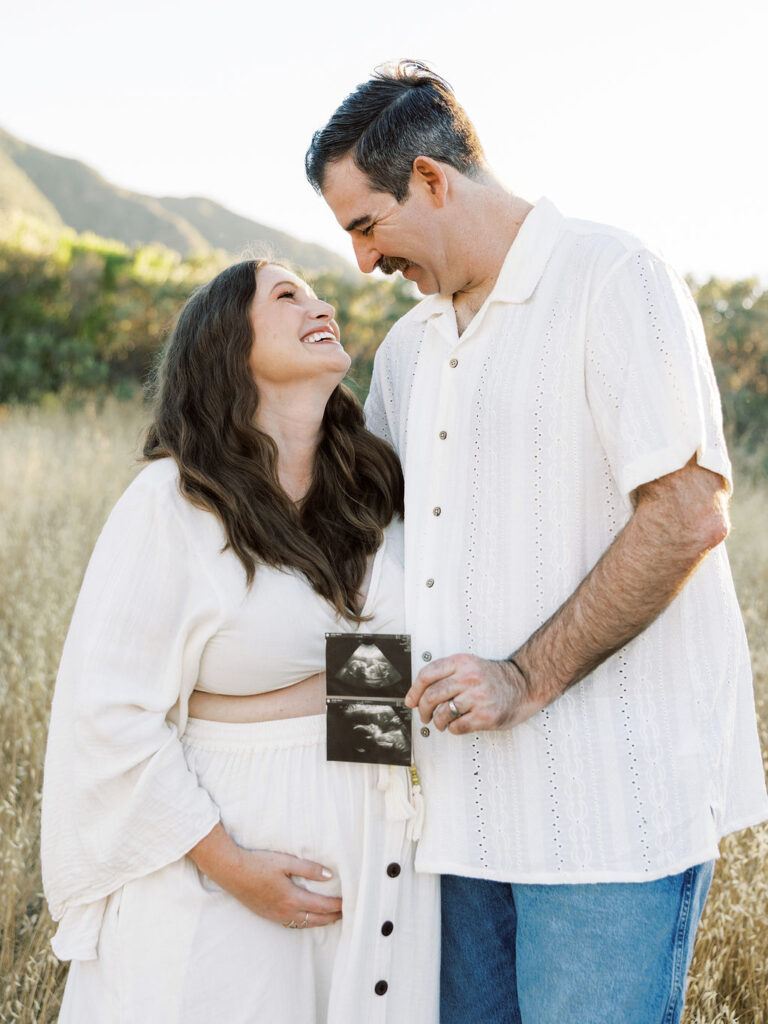 Expecting couple smiling and holding ultrasound photos during a golden hour maternity session in Santa Clarita