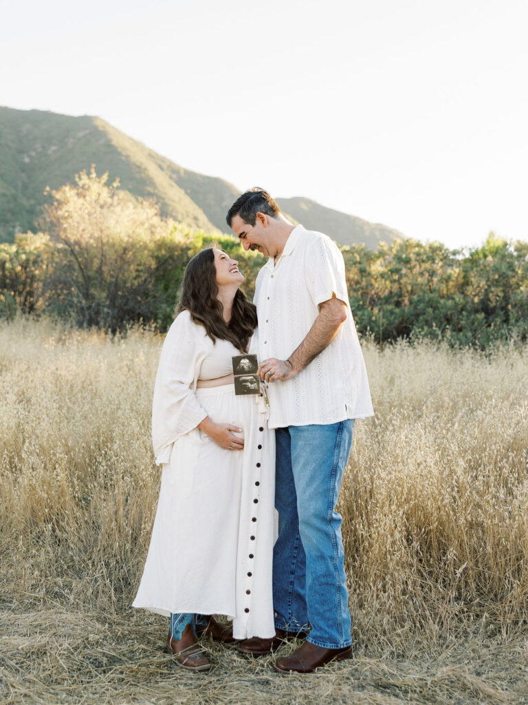 When to Take Maternity Photos with an expecting couple holding an ultrasound photo in a golden Santa Clarita field