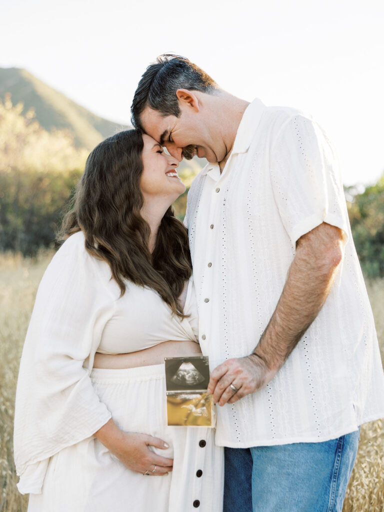 Expecting couple holding an ultrasound photo and embracing during a golden hour maternity session in Santa Clarita