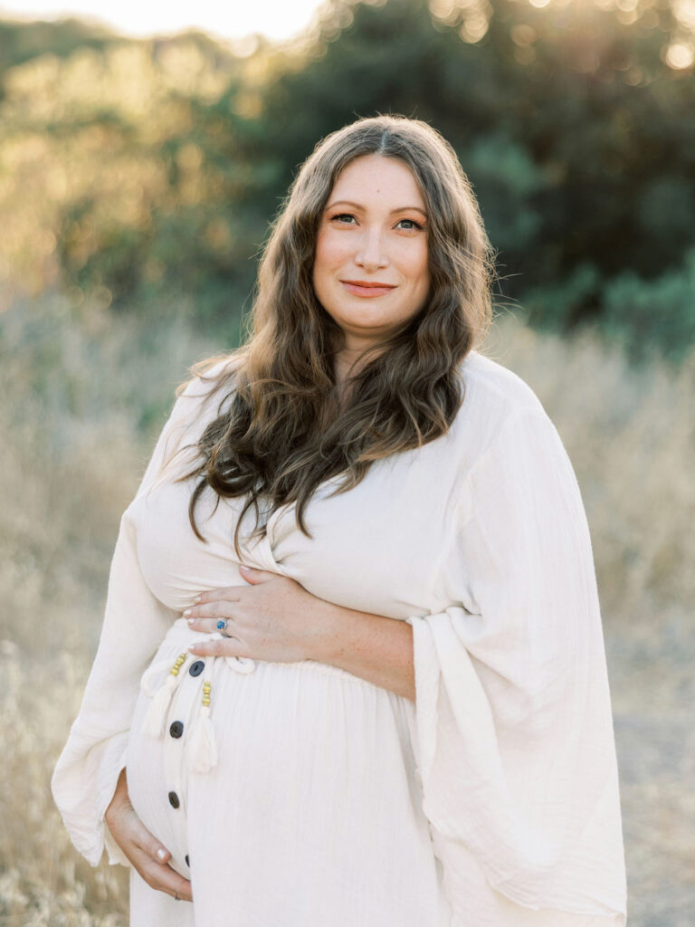 When to Take Maternity Photos with a pregnant woman cradling her belly during a golden hour Santa Clarita maternity session