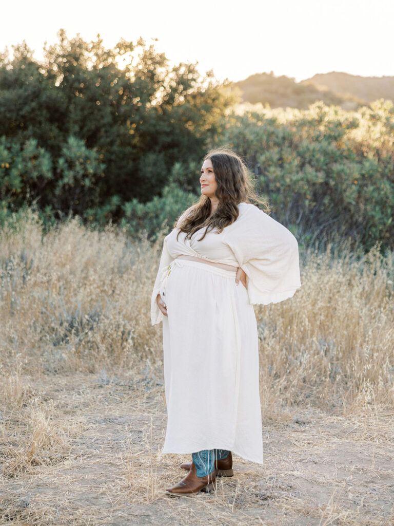 Pregnant woman in a white dress standing in a golden field during a Santa Clarita maternity session