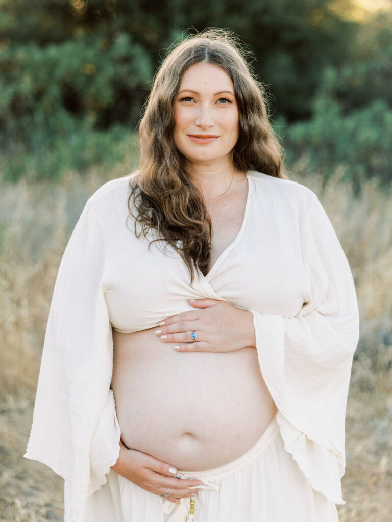 When to Take Maternity Photos with a pregnant woman cradling her belly during a golden hour Santa Clarita maternity session
