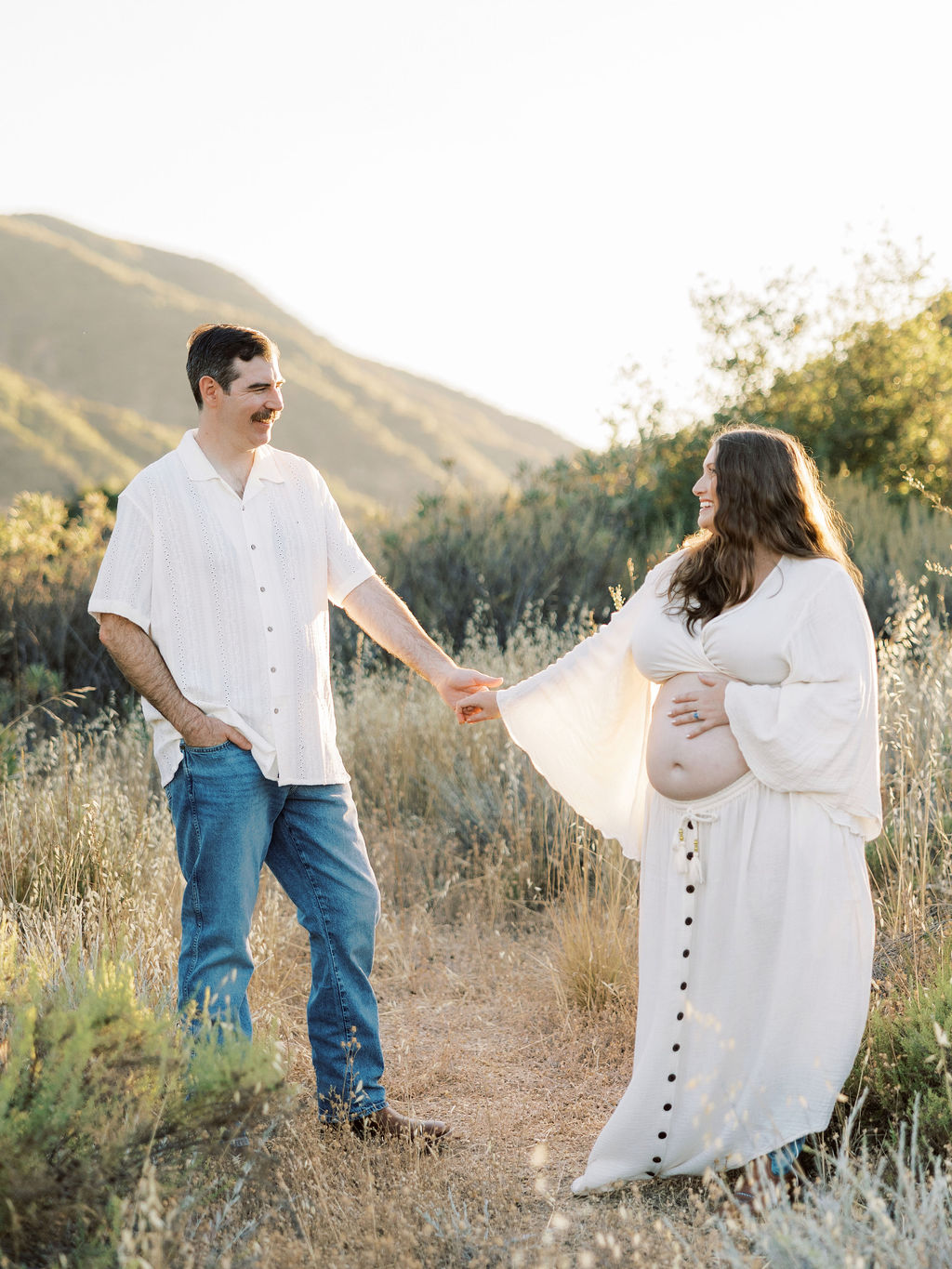 Expecting couple holding hands and smiling during a golden hour maternity session in Santa Clarita