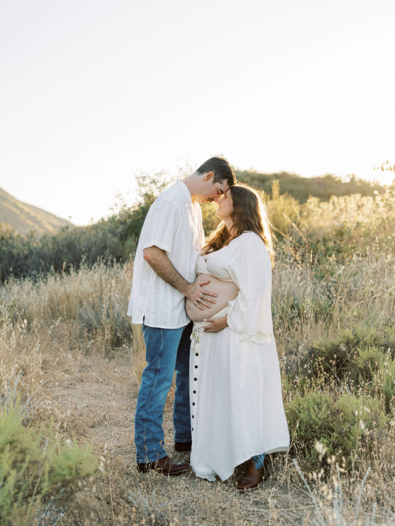 Pregnant couple posing together against soft golden California hills
