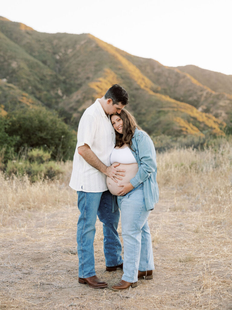 Expecting couple embracing in a sunlit field during maternity photos