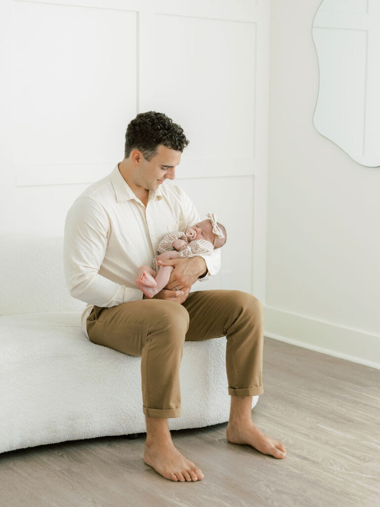 Dad seated while holding his newborn baby during a relaxed studio newborn session