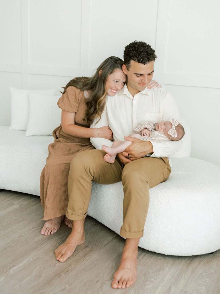 Mom and Dad seated with his newborn baby during a natural studio newborn photography session