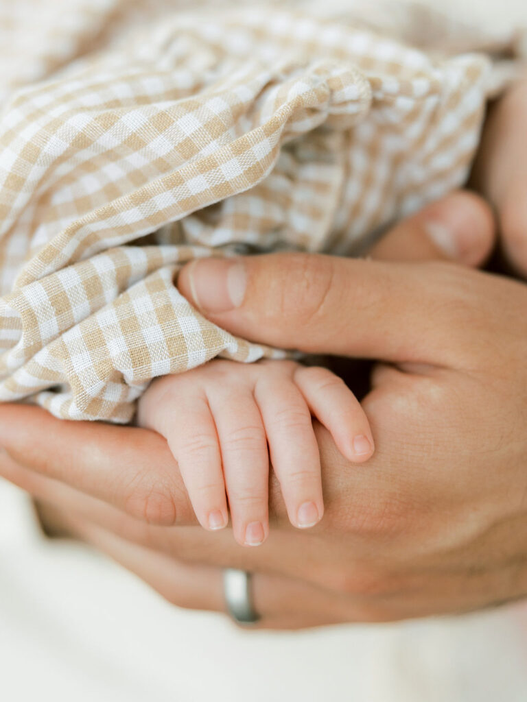 Close up of newborn baby’s tiny hand resting in a parent’s hands