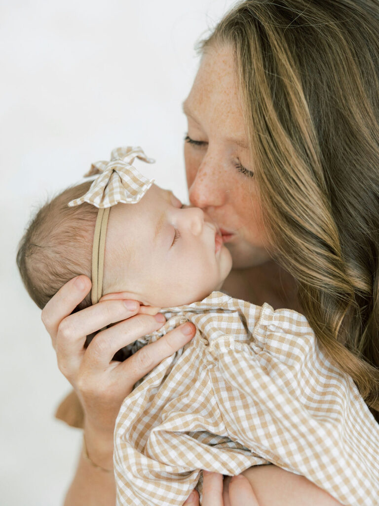 Mom kissing her newborn baby while preparing for newborn photos